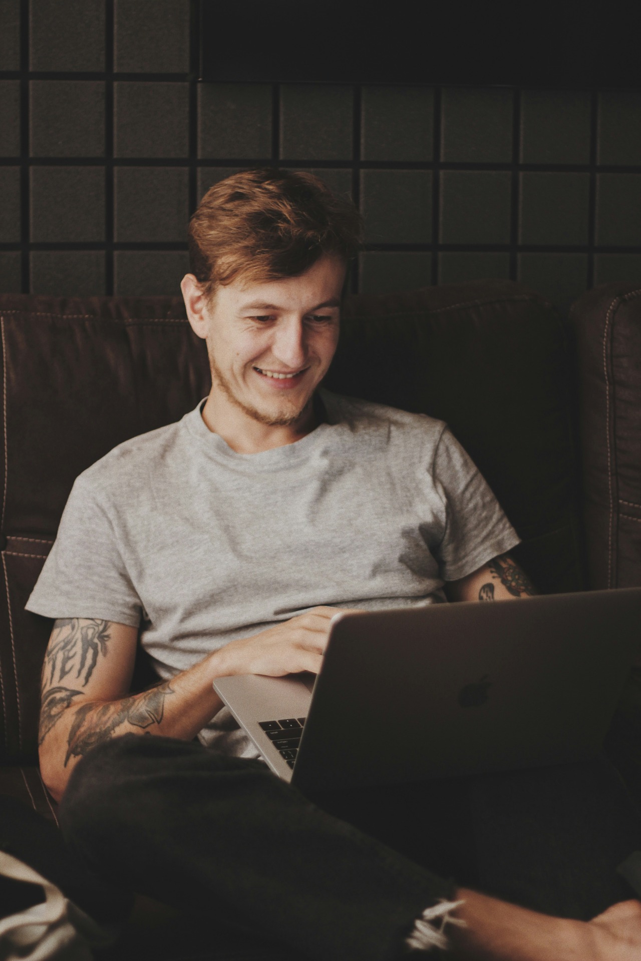 Eine junger Mann der lächelnd auf sein Notebook schaut